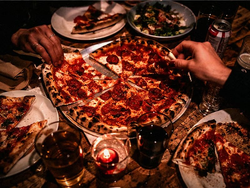 Blick von oben auf den Tisch: angeschnittene Pizza, Gläser und Hände